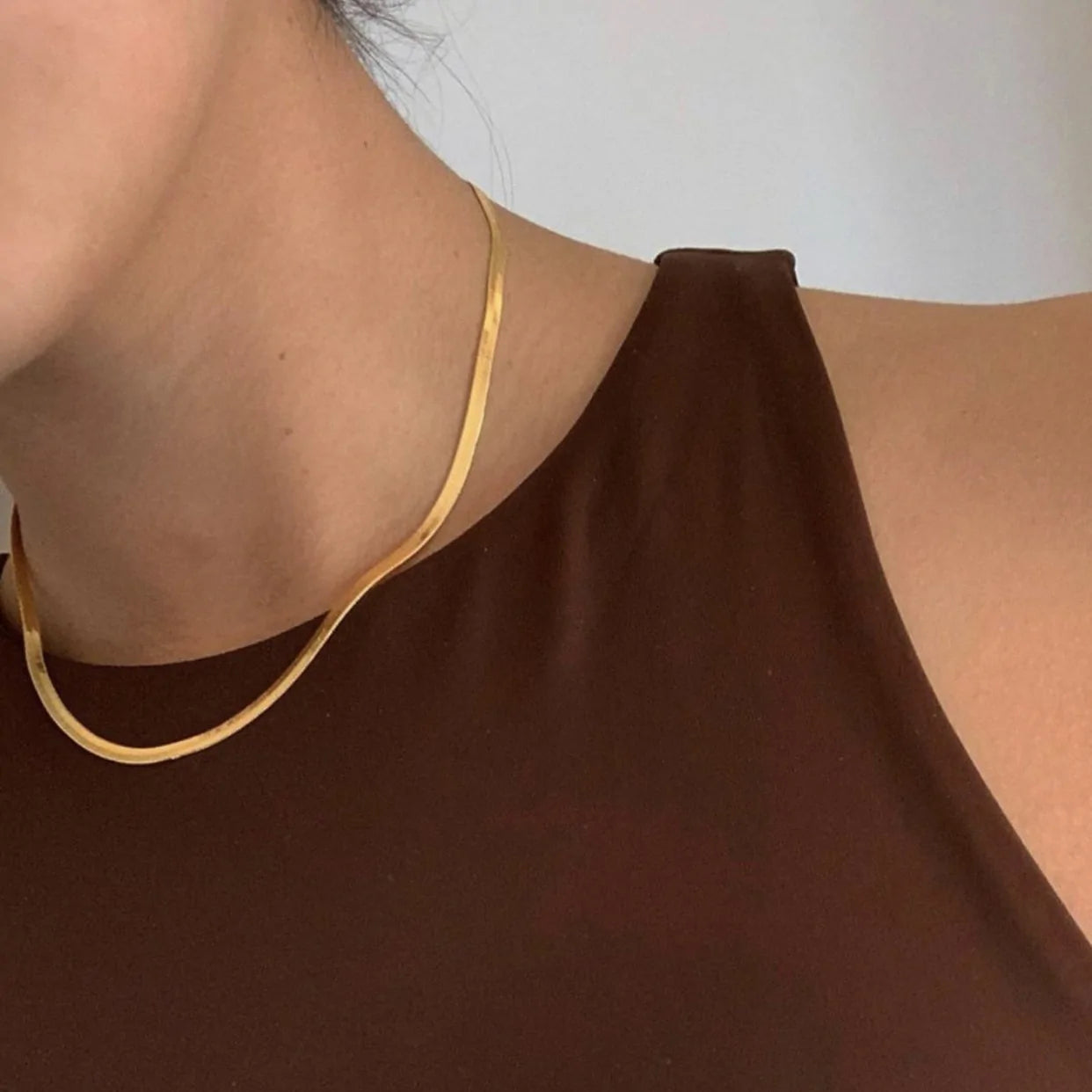 Minimalist styling of the Marisol Shine Necklace, a 24K gold-plated snakebone chain, worn with a brown sleeveless top.