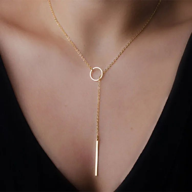 Close-up of the Calista Necklace in gold, featuring a sleek circular pendant and vertical bar drop on a fine chain, ideal for chic outfits.
