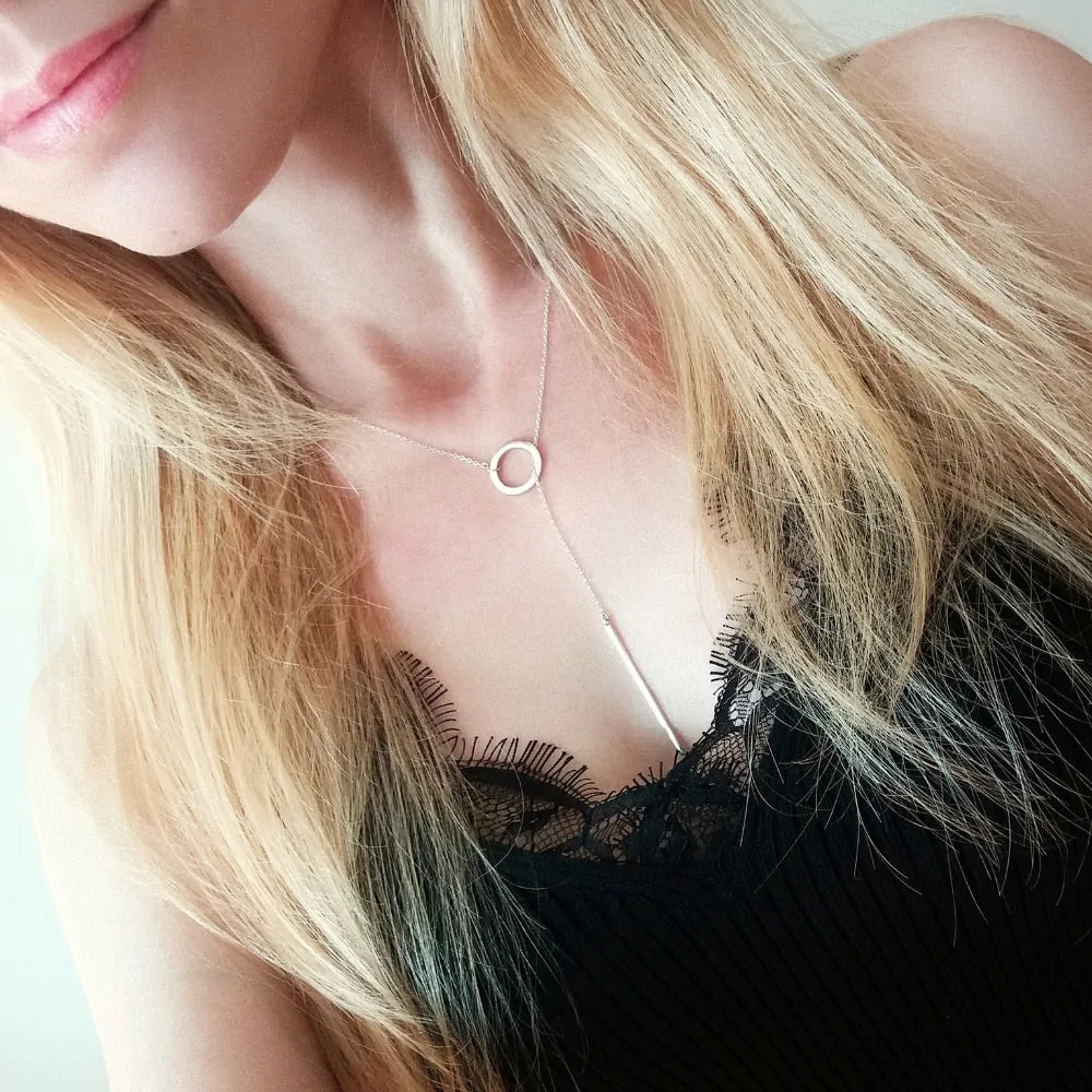 Model wearing the Calista Necklace, showcasing its delicate circular pendant and vertical bar drop against a black lace top.
