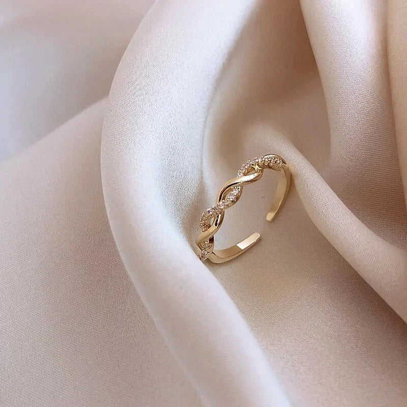 Seraphine Ring displayed on soft beige fabric, showcasing its gold twisted design with embedded crystals for a luxurious and versatile look.