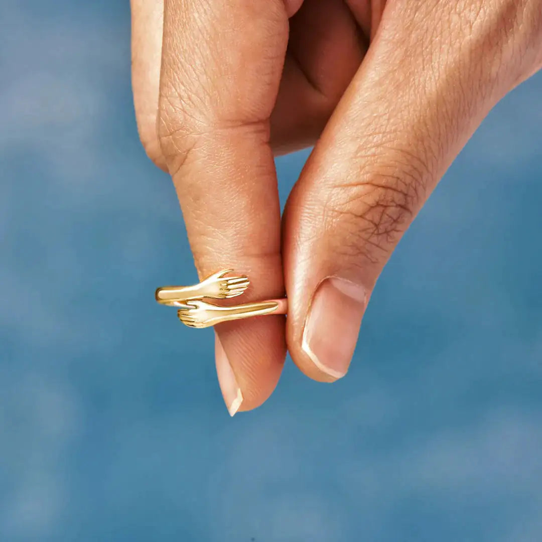 Gold Hug Ring held between fingers, highlighting its intricate design of two hands in an embrace. A perfect gift or everyday accessory.
