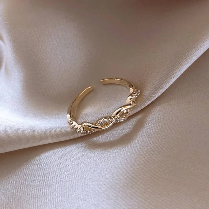 Seraphine Ring placed on beige fabric, featuring a gold twisted design with sparkling crystals, a chic accessory for women.