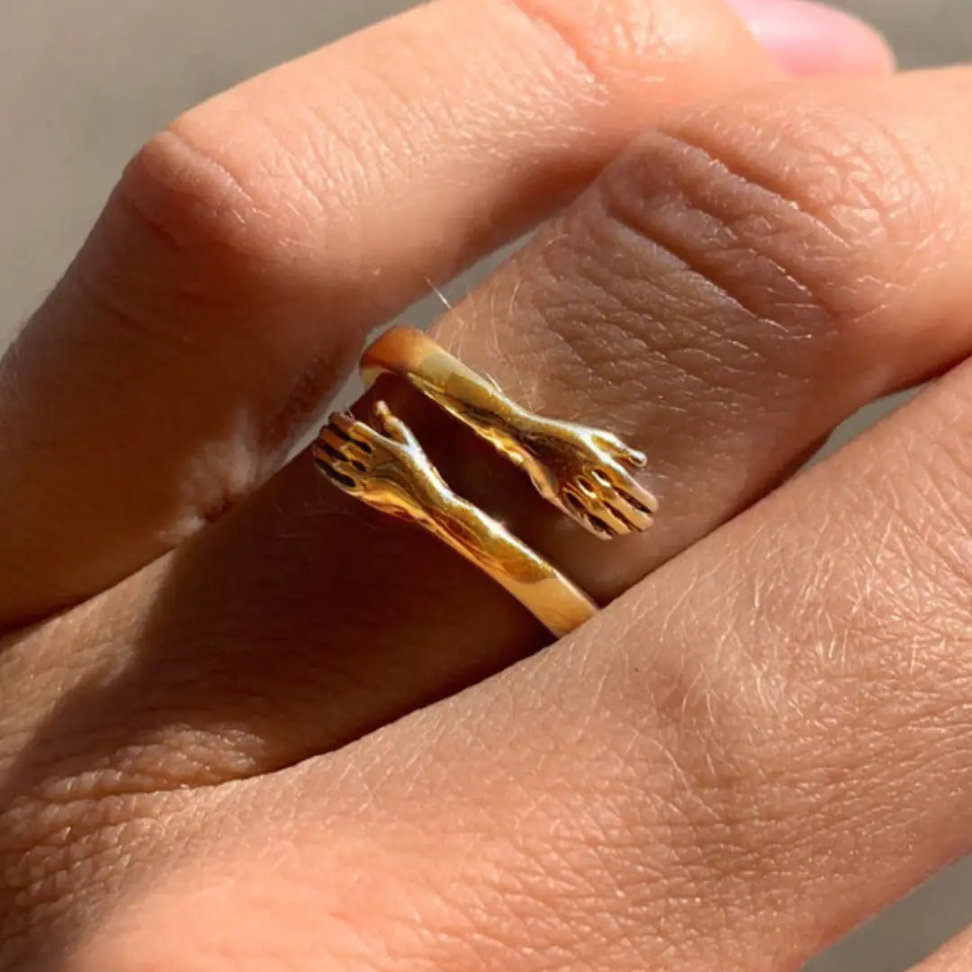 Close-up of a Gold Hug Ring on a finger, featuring two hands in an elegant embrace. A meaningful and stylish jewelry piece.